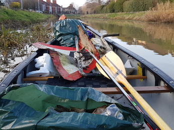 A canoe on a river, filled with rubbish bags.