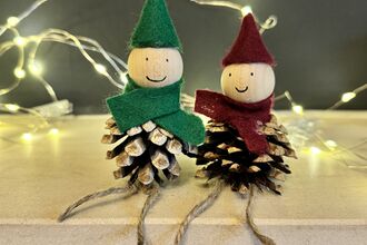 Two elves made out of pinecones set on a shelf, with fairy lights behind them