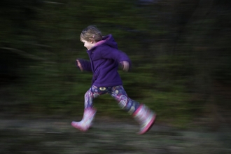 Young girl running in a woodland, wearing wellies