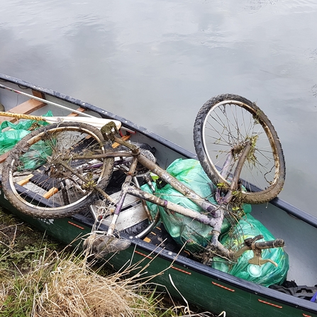 A canoe on the canal filled with rubbish bags and an old bicycle.