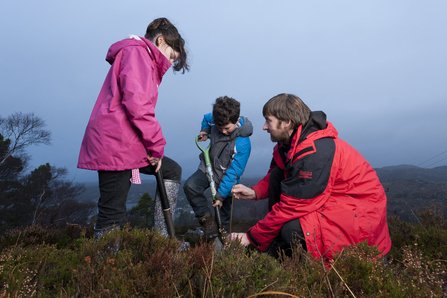 Two children and an adult planting a tree