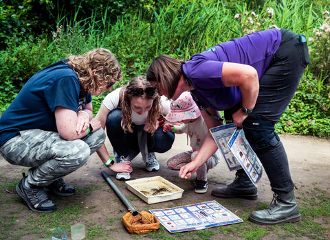 A family examining a tray full of pond creatures