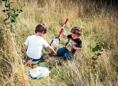 Two children sitting in the grass, holding sweep nets for sampling grassland insects