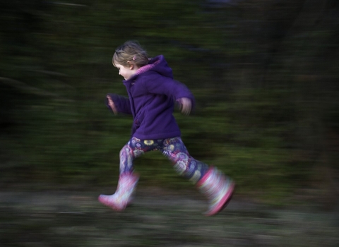 Young girl running in a woodland, wearing wellies